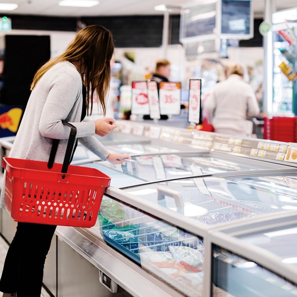 En kvinna som sträcker sig ner i en frys i en matbutik